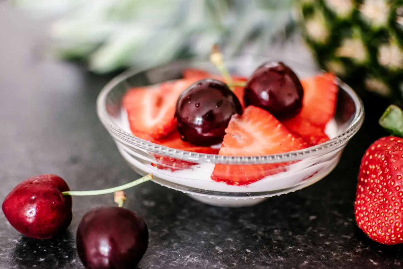 Delicious bowl of yogurt topped with fresh strawberries and cherries.
