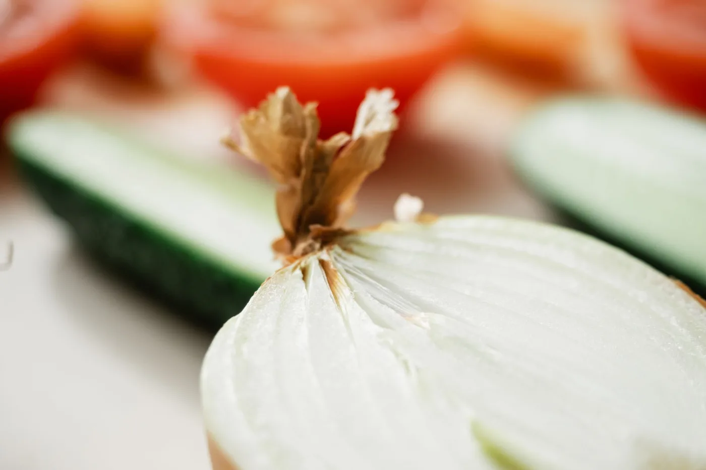 A detailed close-up of a sliced onion with cucumbers and tomatoes in the soft focus background.