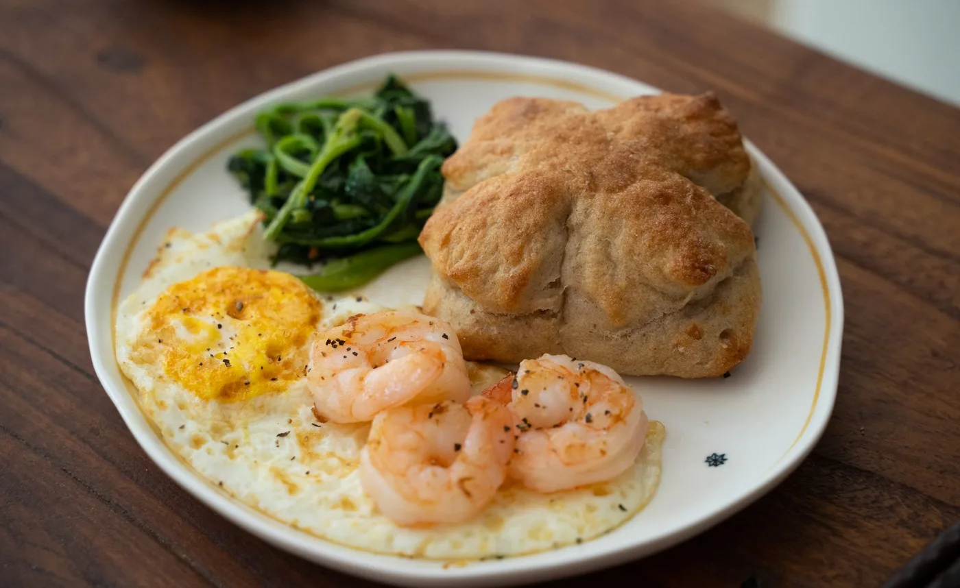 A tasty breakfast plate featuring shrimp, eggs, greens, and bread, perfect for a nutritious start.