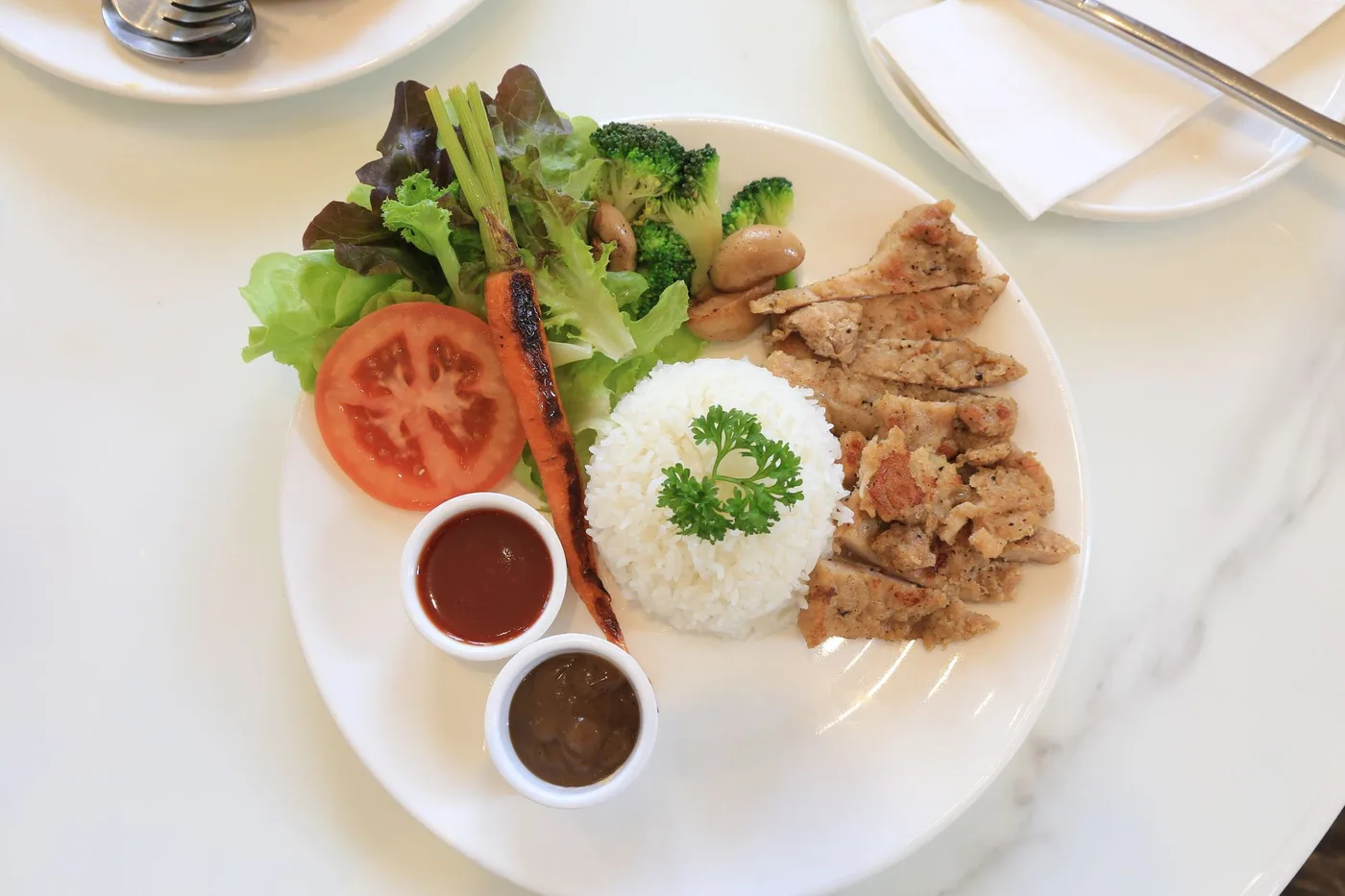 A vibrant plate of grilled chicken, rice, fresh vegetables, and sauces. Perfect for food lovers.
