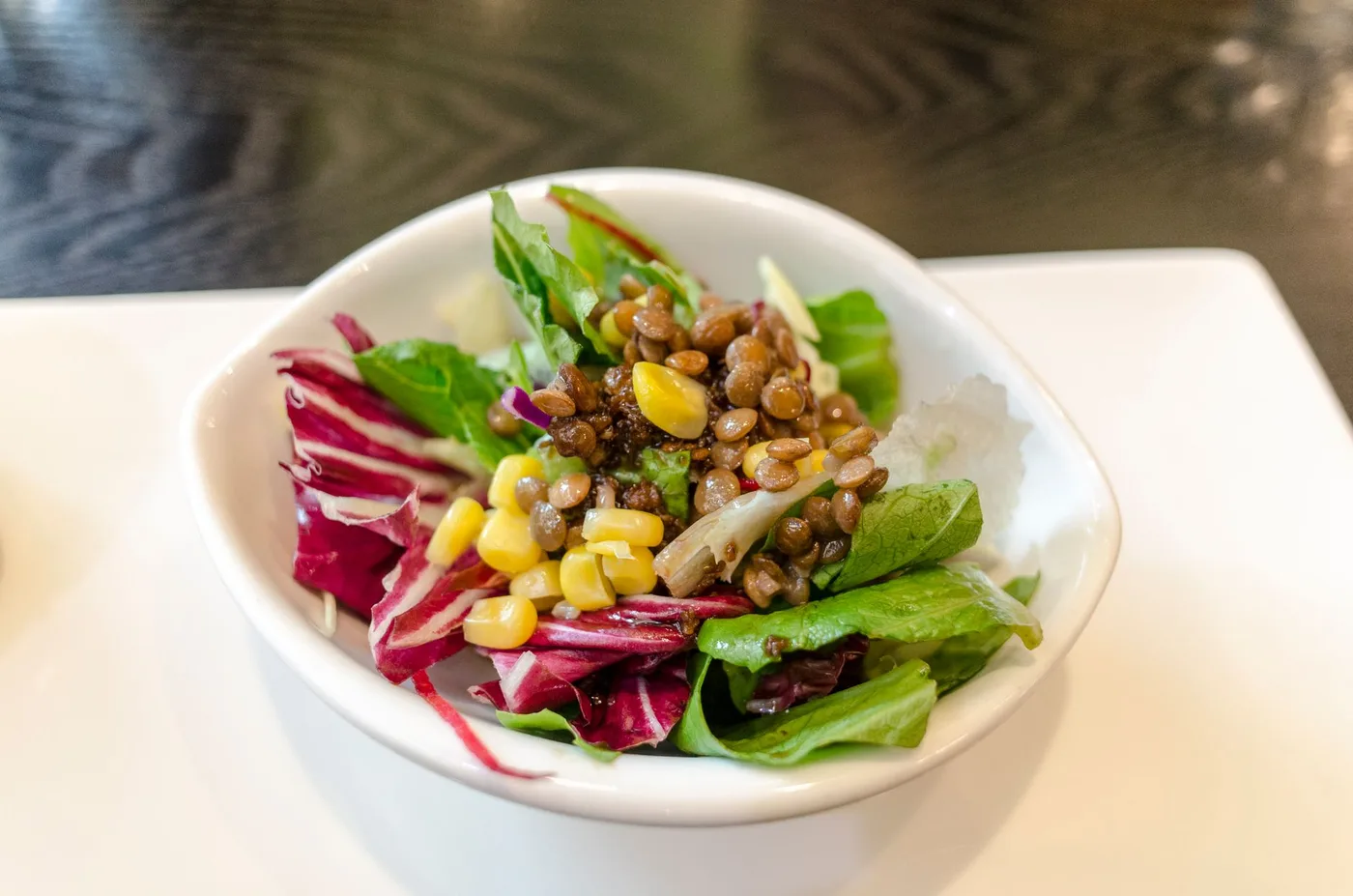 A fresh and delicious vegetable salad featuring lentils and corn served in a white bowl.
