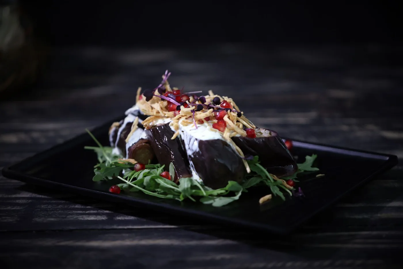 Close-up of a stylishly plated eggplant salad with arugula and pomegranate seeds.