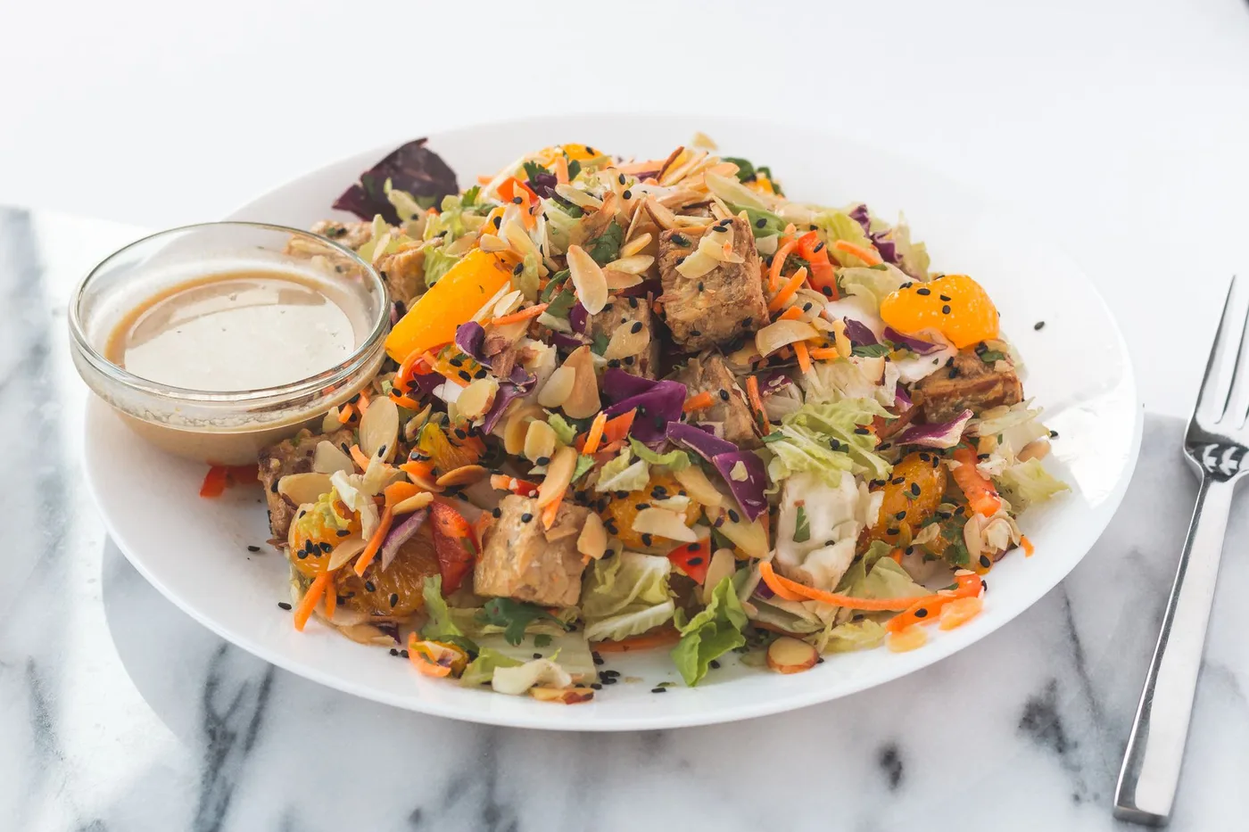 Fresh and vibrant tofu salad with orange slices, almonds, and dressing on the side.