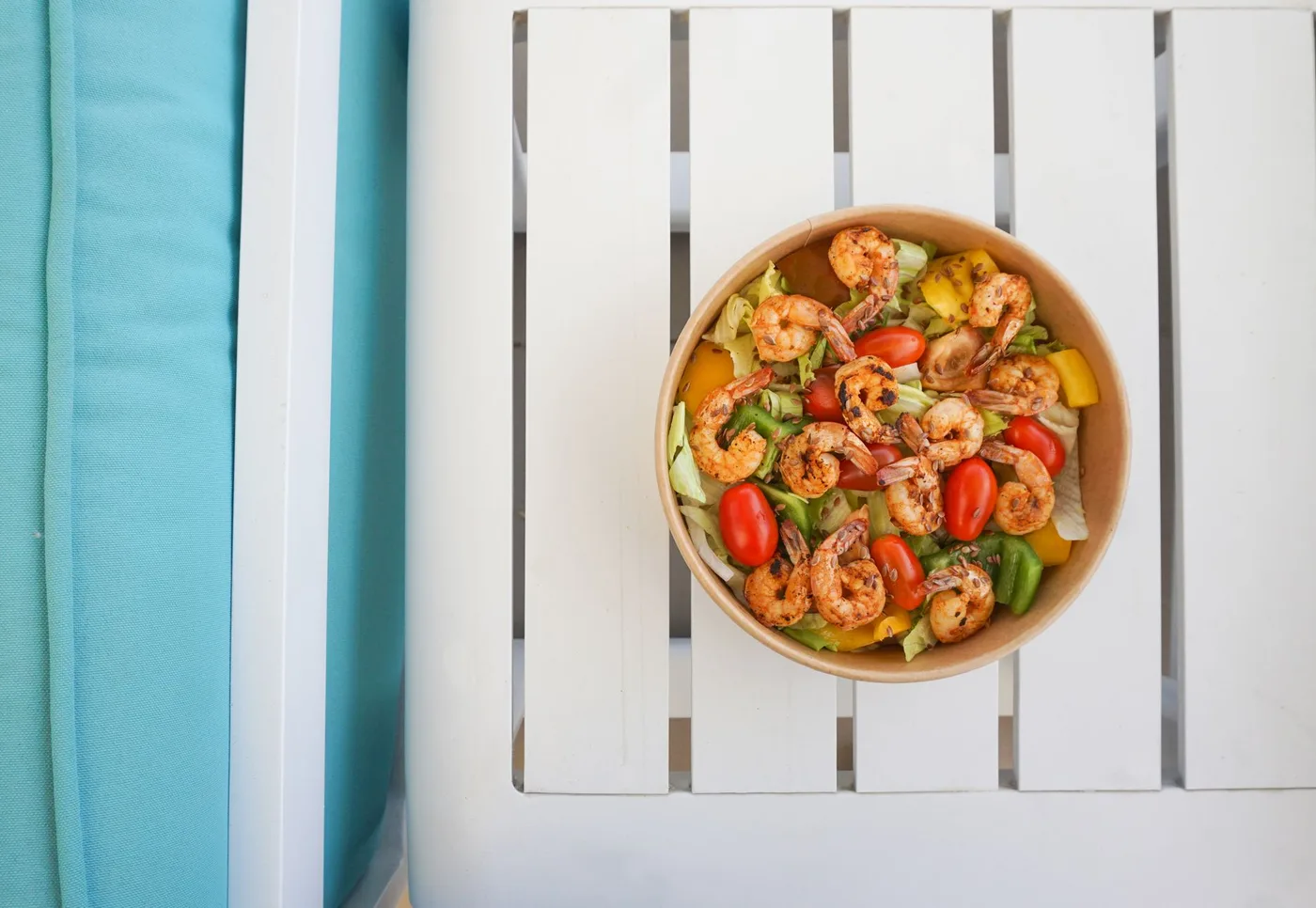 Colorful shrimp salad with vegetables in a brown bowl on a white table, perfect for a healthy meal.