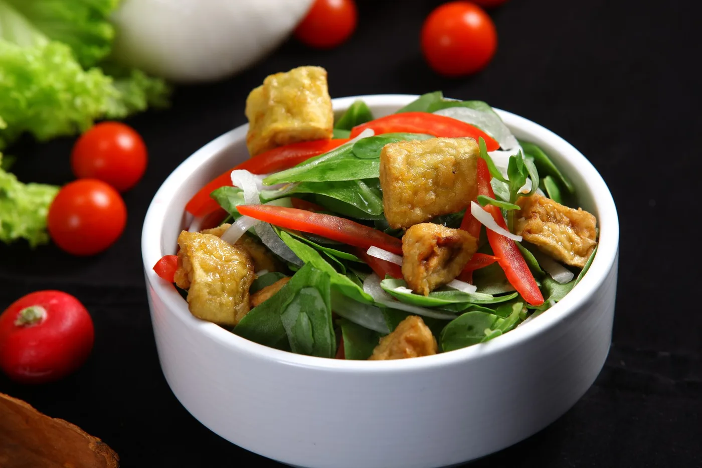 Appetizing vegan salad with tofu and fresh vegetables in a bowl on a black background.