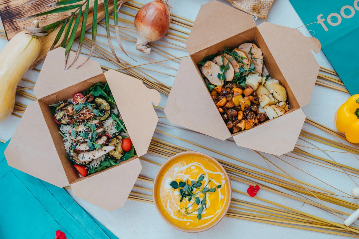 Top view of healthy takeout boxes with salad and soup on a colorful background.