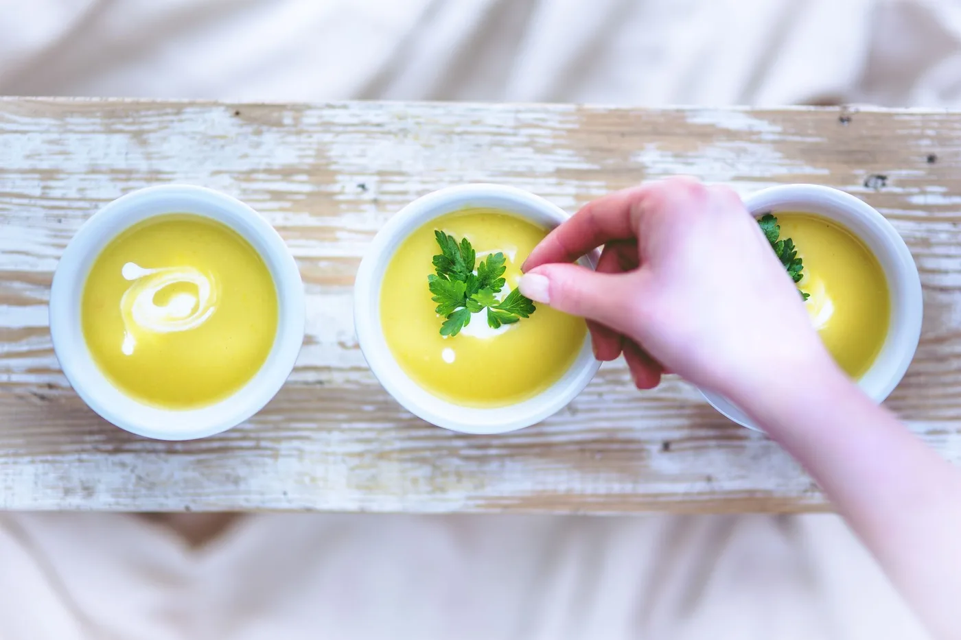 Hand adding garnish to creamy soup bowls, perfect for lunch or dinner.