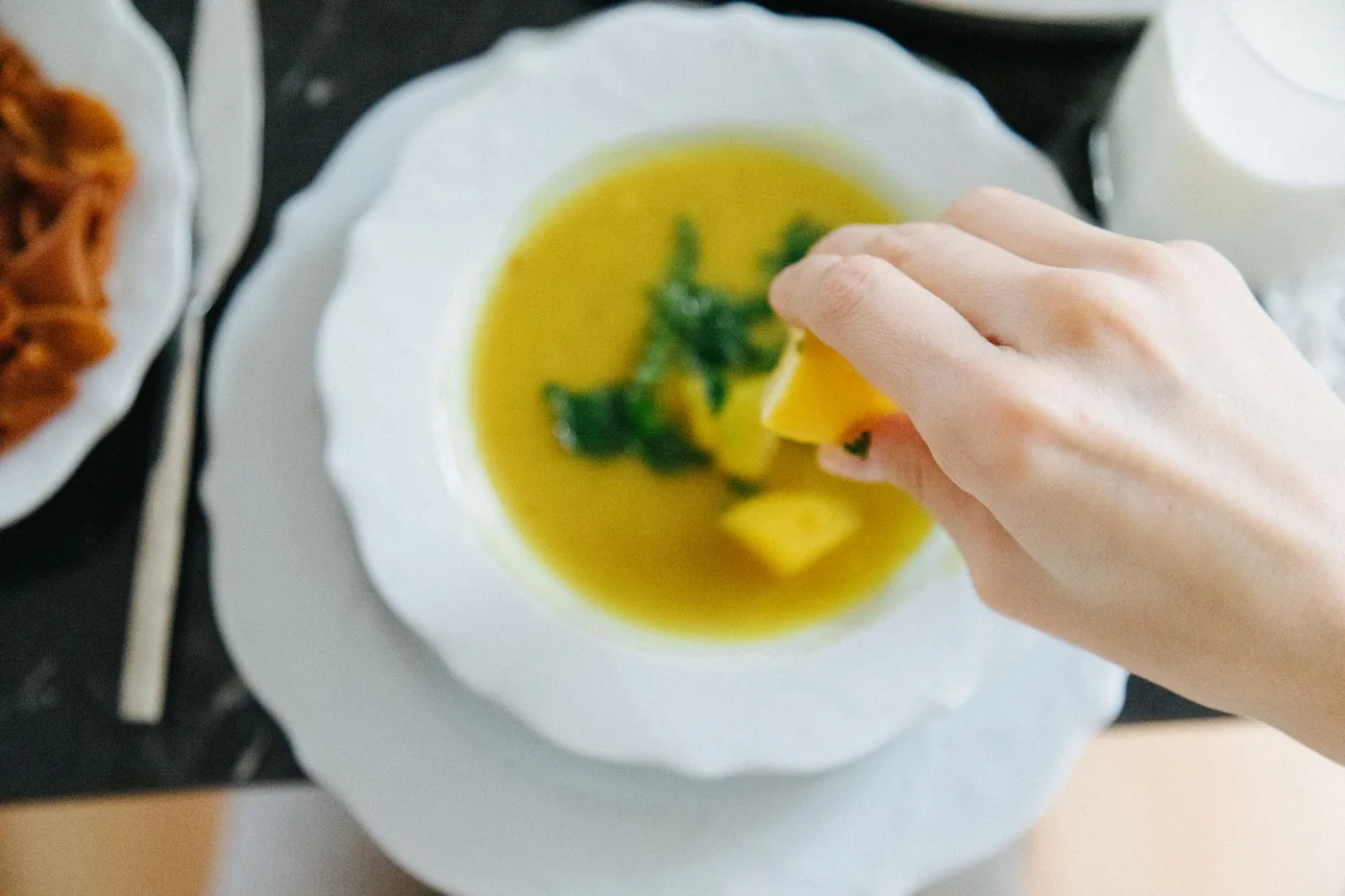 Hand squeezing lemon over lentil soup, enhancing flavor in traditional Turkish setting.
