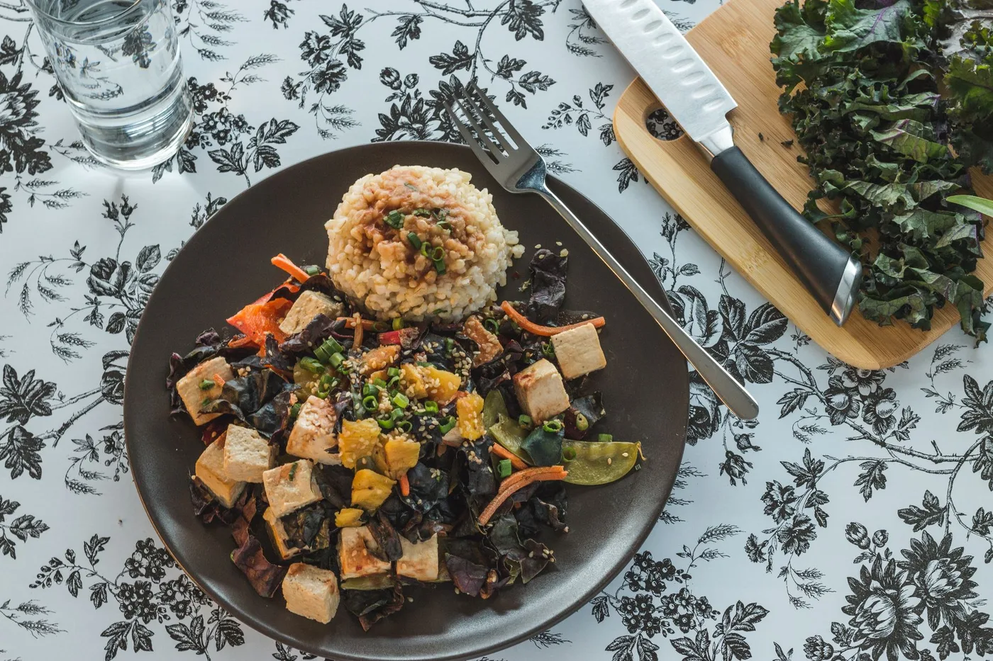 A colorful vegan dish featuring tofu, rice, and fresh vegetables on a stylish table setting.