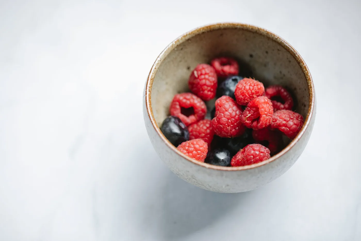 From above organic yummy raspberries and delicious blueberries mixed in ceramic bowl on white table
